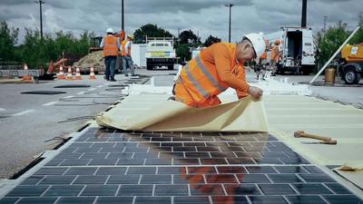 A person laying a solar PV (photovoltaic) panels on a road