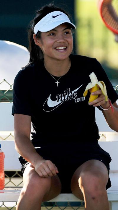 British tennis player Emma Raducanu sitting on a bench and eating a banana