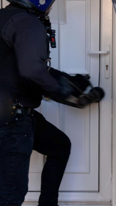 A police officer wearing a helmet and protective clothing bashes a door in.