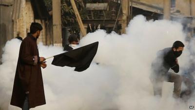 Kashmiri Shiite Muslim protestors take cover as a tear smoke shell explodes during a protest against Saudi Arabia