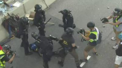 Police hold a protester pinned to the ground while news cameras record it