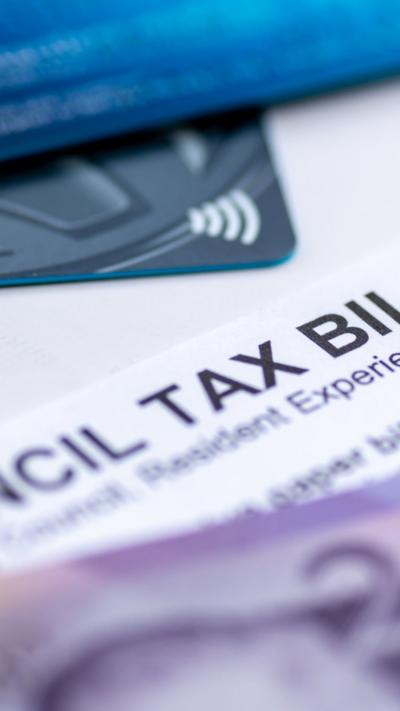 A Council Tax Bill in between Pound Sterling bank notes and bank payment cards.