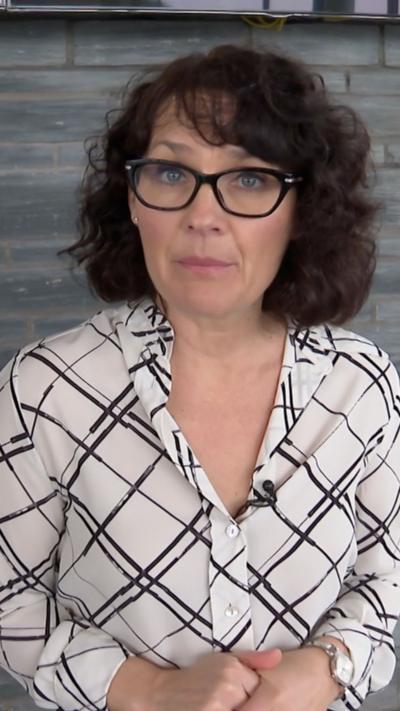 BBC presenter Jennifer Jones looking at the camera. She has black, curly hair and black-framed glasses on. She has a black and white shirt on.