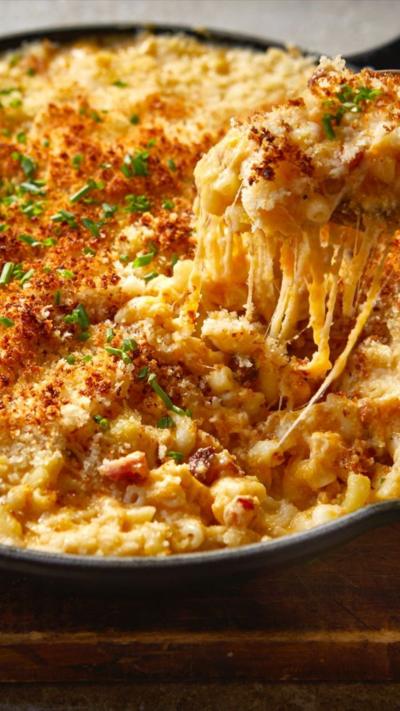 Top down view of a dish with handles full of macaroni cheese. A large spoon is removing some from the dish