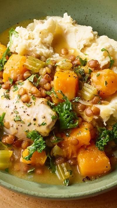 A green bowl containing chicken, butternut squash, potato in a broth.
