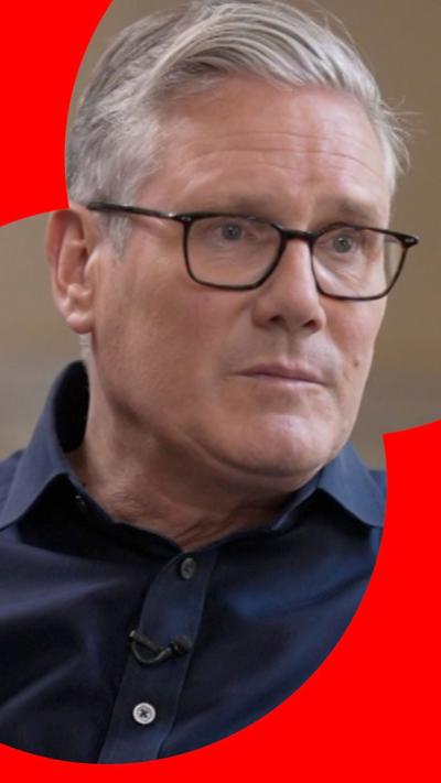 Keir Starmer, with short grey hair and black glasses sits in a chair