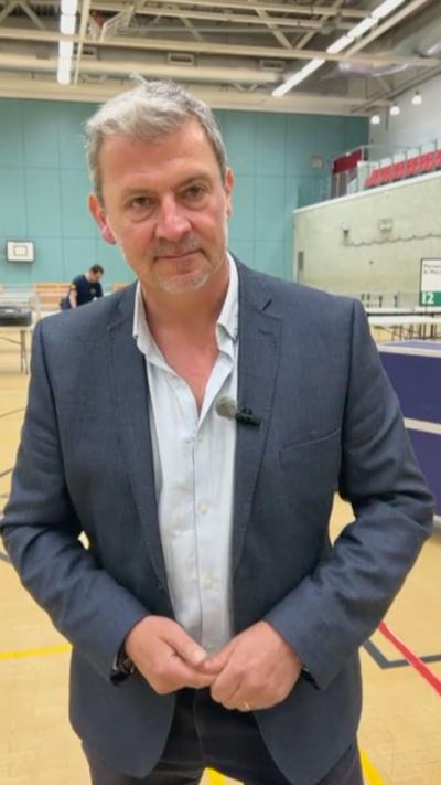 A man wearing a blue suit with a light blue top. 
