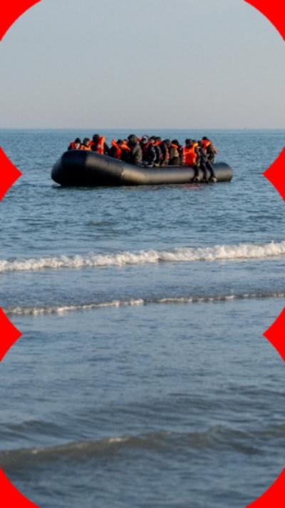 A inflatable boat at sea with migrants onboard wearing orange life jackets.