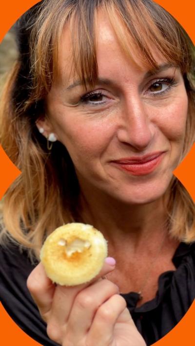 A woman with light brown hair, holds a mushroom and smiles at the camera.