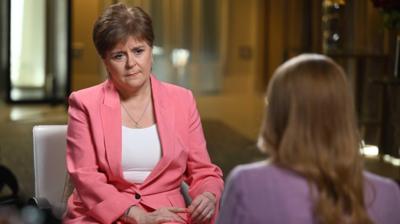 Nicola Sturgeon wearing pink suit and white t-shirt facing blonde woman wearing lilac blazer