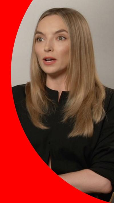 A woman with straight blond hair wearing a black top, sitting down.