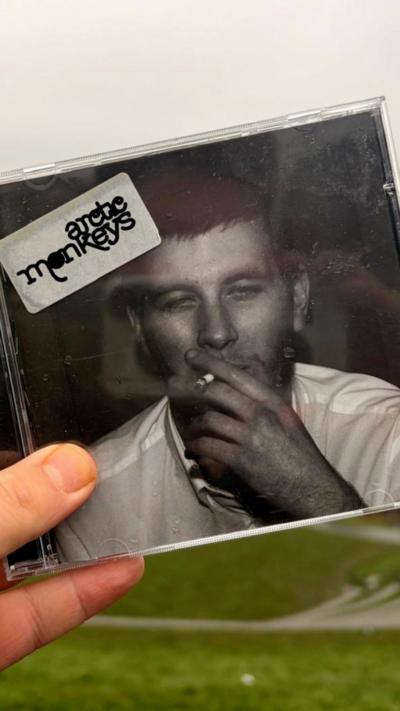 A copy of the Arctic Monkeys' debut album held in someone';s hand. The cover image of the CD shows a man with short cropped hair smoking a cigarette