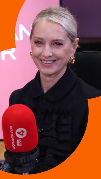 Katherine LaNasa has blonde hair pulled away from her face. She sits in front of a microphone and smiles at the camera.