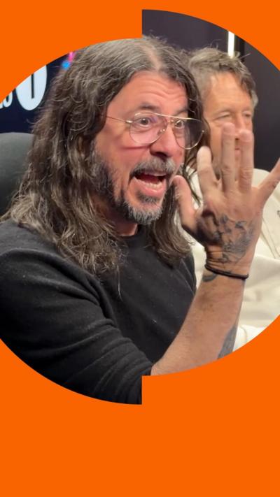 A man, Dave Grohl, in a black t-shirt holding hands in front of his face.