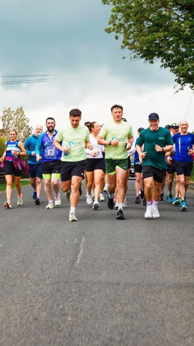 A group of people running a marathon along a country lane
