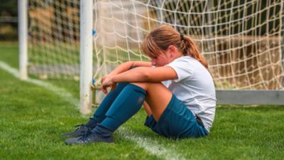 Girl sitting in a football goal looking sad.