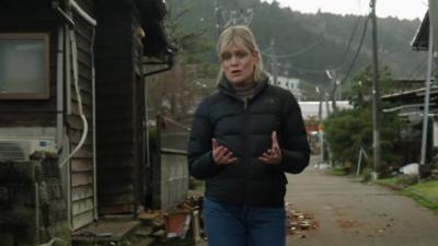 Jean MacKenzie walks along road with damaged buildings on either side