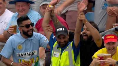 Security guard in high-viz vest waves in the air amongst crowd in the cricket stand