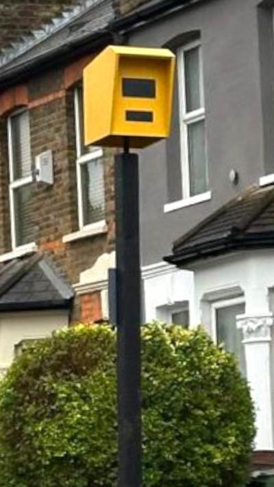 Fake yellow speed camera in a planter next to a row of houses