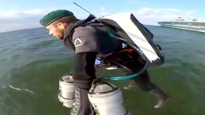 A man wearing a jet suit flying above open water