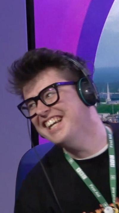 Young man wearing glasses and headphones is mid laugh.