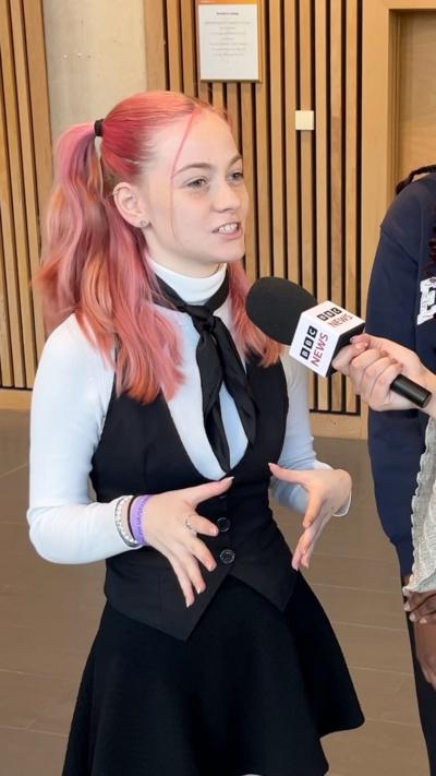 A teenage girl speaks into a BBC News mic. She has pink hair in pigtails and wears a black and white outfit