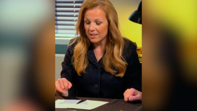 A woman in a black outfit with long hair looks down at two pieces of paper