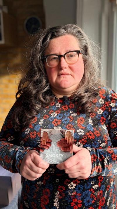 A woman in a flower dress holds a picture of her babies hands.