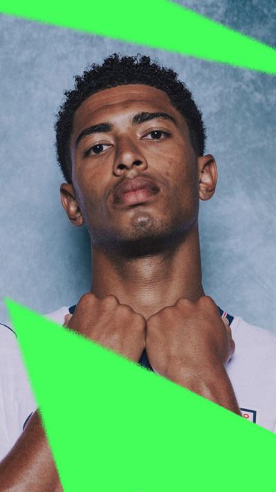 Jude Bellingham poses with his fists under his chin, wearing England kit in front of a blue background