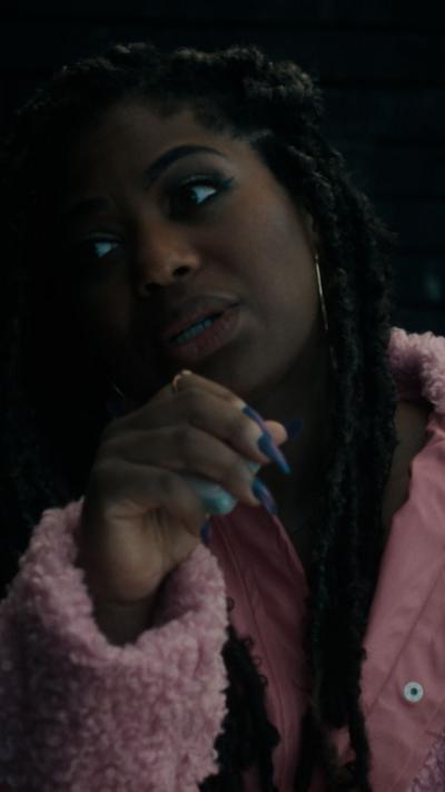 Alternative description
Sharla is speaking, her hand is partly in front of her face, she is wearing a pink coat
