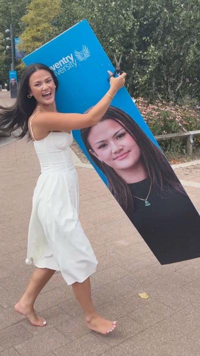 A woman in a white dress holding on to a blue cardboard cutout of her face