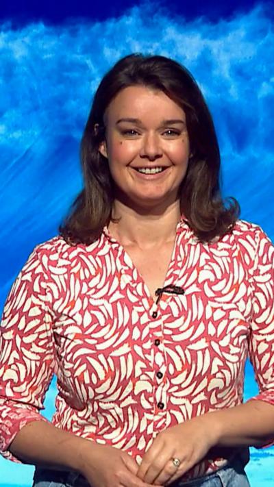 Gillian Smart has shoulder length dark hair, wears a patterned shirt and jeans