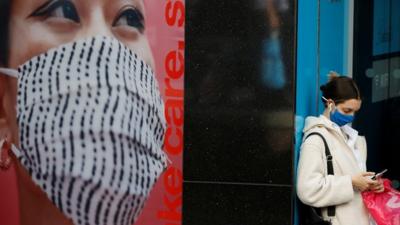 Woman in mask stands next to poster of woman wearing mask