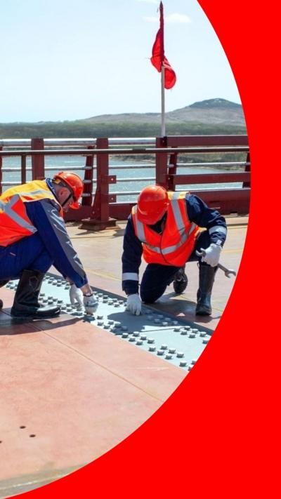 Two men in orange hard hats and high vis jackets inspect rivets on a road bridge connecting North Korea and Russia.