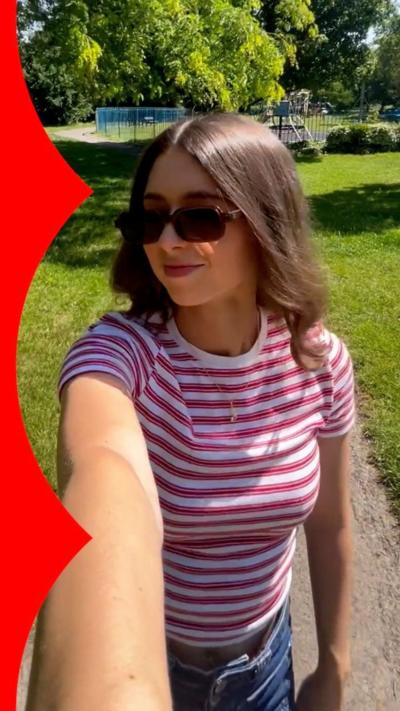 Selfie view of a woman outside wearing sunglasses and stripy top, in a park