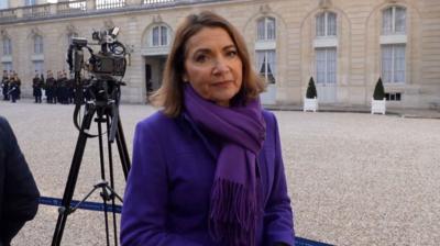 Katya Adler standing outside the Elysee palace in Paris. She is wearing a purple scarf and coat 