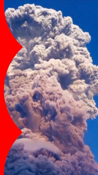 A giant plume of ash rises against a blue sky.