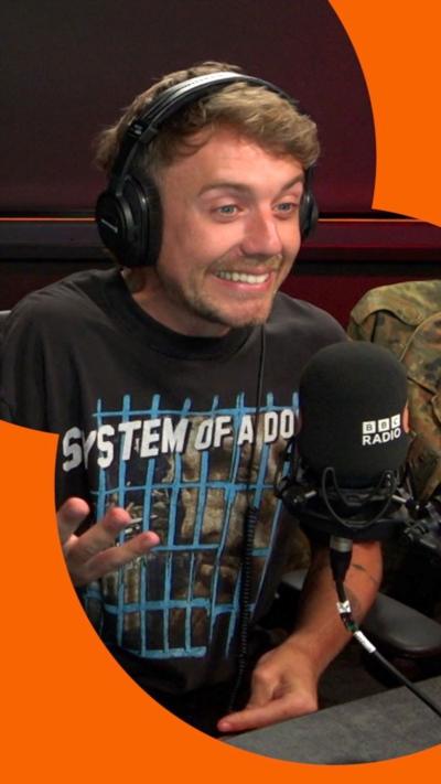 Roman Kemp in the BBC Radio 2 studio. He wears Headphones and a black tshirt