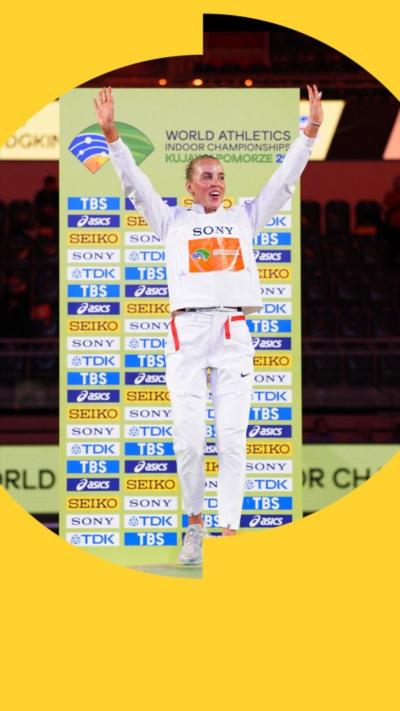 Keeley Hodgkinson wears a white tracksuit and stands on a podium with her arms raised