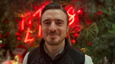 A man in a black puffer jacket and grey top