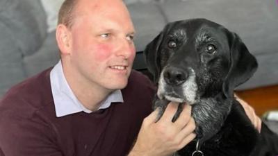 Sean Dilley smiling in his living room with his guide dog, Sammy