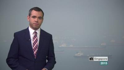 Still from weather presenting video - Ben Rich with hazy photograph from Singapore in the background