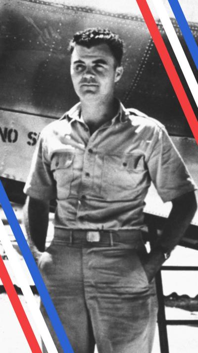 A black and white photo of Hiroshima mission pilot Paul Tibbets stood in front of the shiny silver Enola Gay plane, which he flew to drop the atomic bomb on Hiroshima. In the picture he is young, has short dark hair and is wearing a raggedy shirt with the top buttons undone, holding his hands behind his back.
