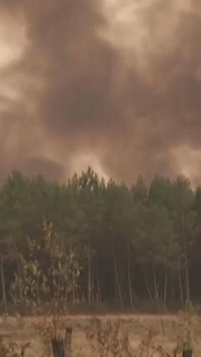 The sky is filled with black smoke above forestry/farmland