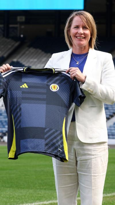 New Scotland head coach Melissa Andreatta in a white suit holding a Scotland top.