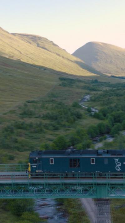 A green locomotive crosses a bridge in the Scottish Highlands