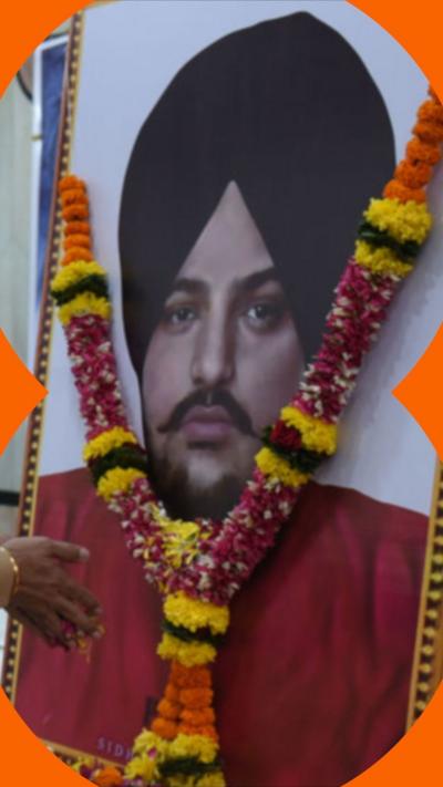 An image of Sidhu Moose Wala on a wall, with a garland of flowers pinned to it.