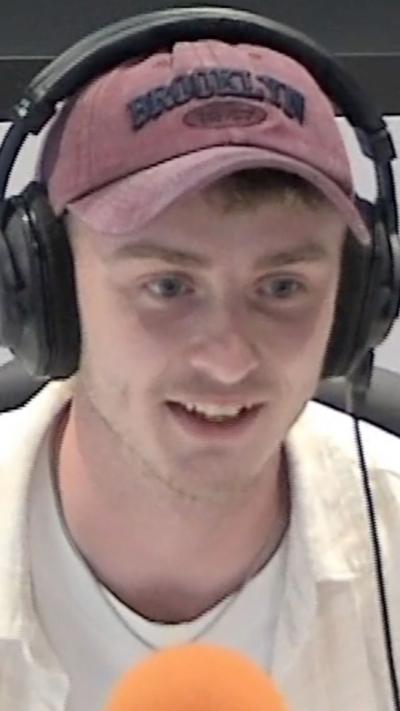 Actor Sam Locke in a red cap that says Brooklyn on it in black letters and black over-ear headphones