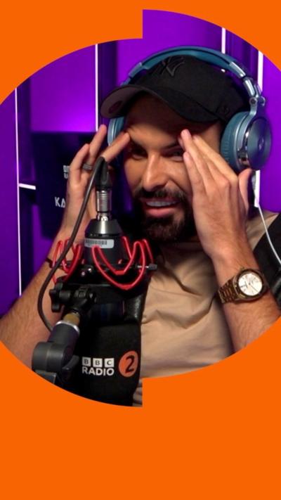 Rylan looks shocked in a purple-lit radio studio