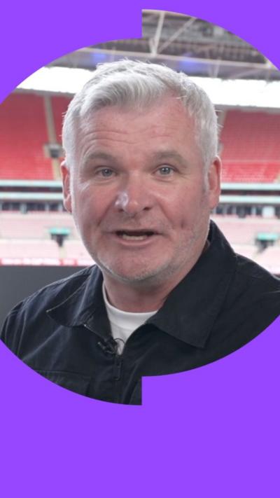 Guy Mowbray has short grey hair. He is wearing a white T-shirt under a dark-coloured overshirt with a collar.
